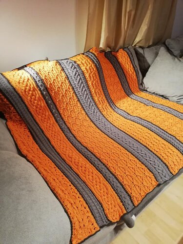 Gehäkelte Decke mit orange-grauen Streifen und reliefartigem Muster auf einem Sofa