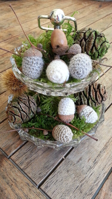 Herbstliche Etagere mit gehäkelten Eicheln, Tannenzapfen und Moos auf einem Holztisch.