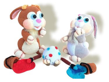 Two crocheted amigurumi rabbits with a polka-dot crochet egg and red and blue paint pots