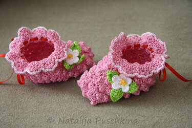 Rosa gehäkelter Babyschuh mit Rüschenrand, rotem Band und weißer Blume