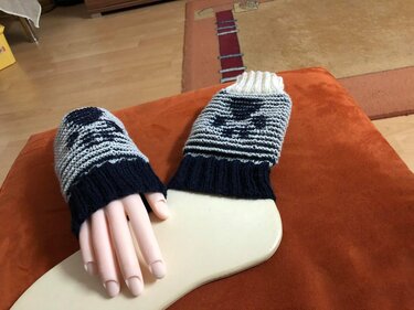 Zwei gestrickte Stulpen mit Muster in Dunkelblau, Hellgrau und Creme auf Handformen.