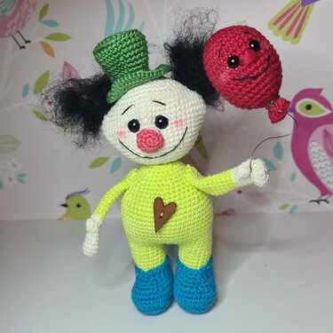 Gehäkelte Amigurumi-Clownpuppe mit weißem Gesicht, schwarzem Kraushaar, grünem Zylinder und rotem Ballon