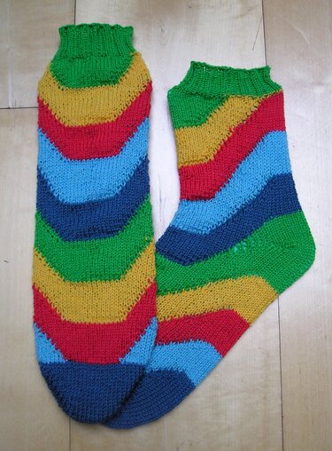 Ein Paar gestrickter Damensocken mit bunten diagonalen Zickzackstreifen und Rippbündchen, liegend auf hellem Holz