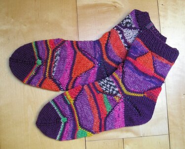 Bunte handgestrickte Damensocken mit geometrischem Muster auf hellem Holzboden
