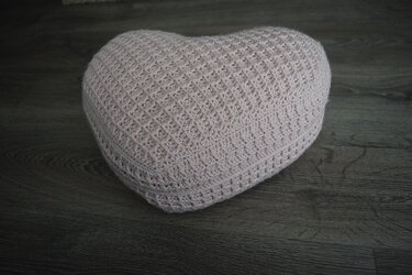 Gehäkeltes Herzkissen in zartem Rosé mit Waffelmuster auf dunklem Holzfußboden