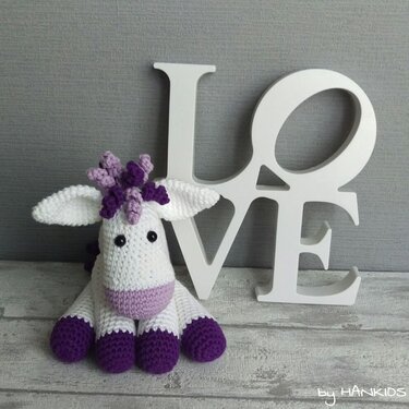 Gehäkeltes Einhorn-Amigurumi in Weiß und Lila vor weißen LOVE-Buchstaben