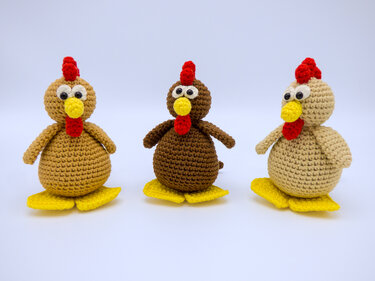 Drei gehäkelte Amigurumi-Hühner in beige, braun und hellbraun mit gelbem Schnabel und Füßen