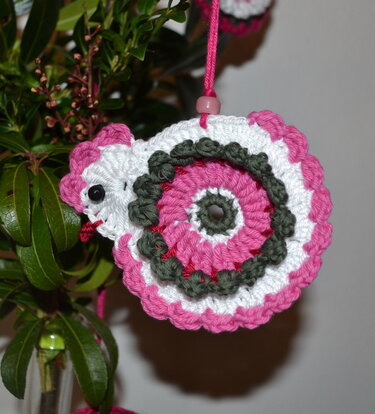 Gehäkelter Schnecken-Anhänger in Rosa, Weiß und Grün an einer Schnur hängend