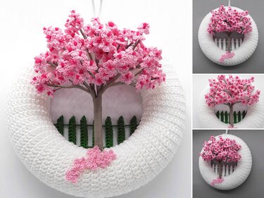 White crocheted wreath with a pink cherry blossom tree and miniature picket fence.