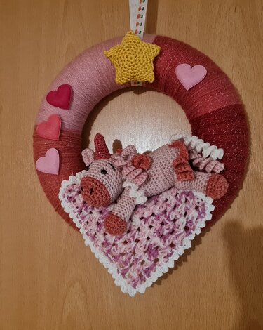 Runder Türkranz in Rosa- und Rottönen mit gehäkeltem liegendem Einhorn auf Herzdecke, Filzherzen und gehäkeltem gelben Stern.