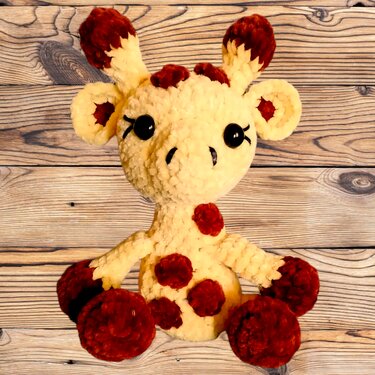 Sitzende Amigurumi-Giraffe mit runden Pfoten, cremefarben und rostbraunen Punkten