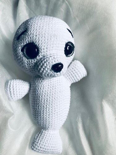White crochet amigurumi seal with black safety eyes on light fabric