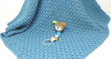 Blaue gestrickte Babydecke mit Flechtmuster und kleinem Stofftier
