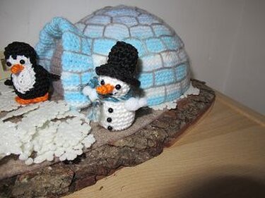Gehäkeltes weiß-blaues Iglu mit gehäkeltem Pinguin und Schneemann auf einer Holzscheibe
