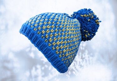 Blau-gelbe gestrickte Bommelmütze vor hellem Hintergrund