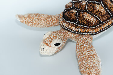 Crocheted amigurumi sea turtle with brown, white, and black patterned shell and light brown body.