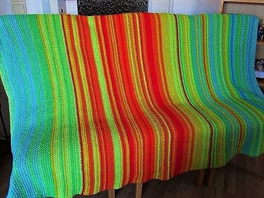 Gehäkelte Decke mit vertikalen Streifen in leuchtenden Blau-, Grün-, Gelb-, Orange- und Rottönen.