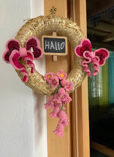 Strohkranz an einer Tür mit pinken gehäkelten Blumen, Schleifen und einer kleinen Kreidetafel 'HALLO'.