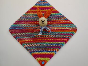 Handgestricktes Schmusetuch mit Regenbogenstreifen, angenähtem Hasenkopf, orangen Ohren und blauem Schal