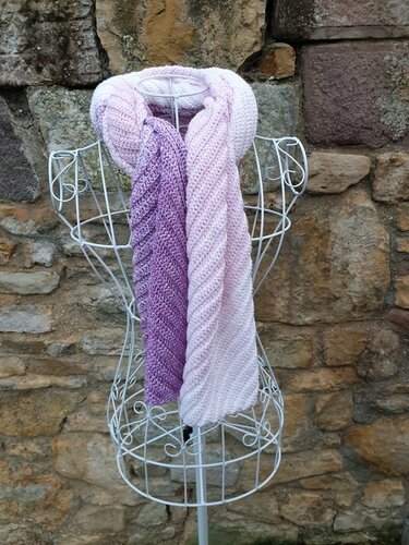Gehäkelter Farbverlaufsschal (Lila-Rosé) mit Diagonalmuster auf weißer Drahtbüste vor Steinmauer