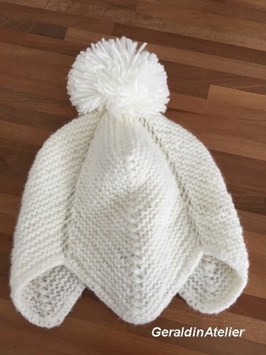 Weiße gestrickte Babymütze mit Bommel auf Holzuntergrund