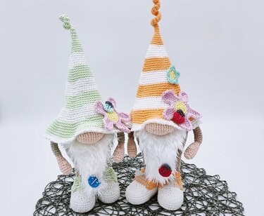 Zwei gehäkelte Amigurumi-Wichtel mit gestreiften Zipfelmützen und Blüten