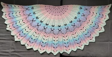 Halbrundes gehäkeltes Tuch in Pastellfarben mit Lochmuster auf dunklem Hintergrund