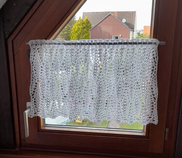 Weiße gehäkelte Scheibengardine mit Blatt- und Spitzenmuster an Holzfenster