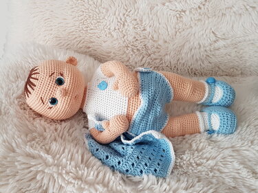 Gehäkelte Amigurumi-Puppe in Blau und Weiß auf flauschiger Decke.