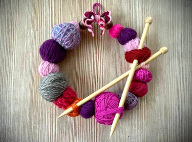 Kranz aus bunten Wollknäueln mit gekreuzten Stricknadeln und Häkelschleife