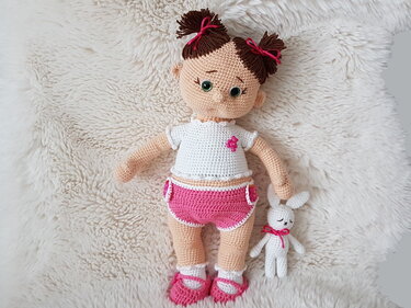 Gehäkelte Amigurumi-Puppe in Weiß und Pink mit kleinem Häkelhasen auf flauschigem Untergrund