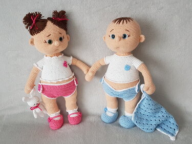 Zwei gehäkelte Amigurumi-Babypuppen, Mädchen in Rosa mit Hasen und Junge in Blau mit Decke, auf grauem Hintergrund