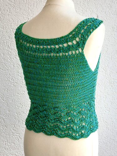 Rückansicht eines gehäkelten Damen-Tops in Grün-Blau mit Lochreihen an den Schultern und Wellensaum auf einer Schneiderpuppe.