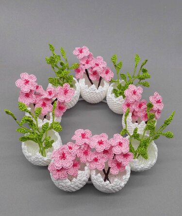 Easter crochet wreath of pink flowers in white eggshell crochet planters on a gray background