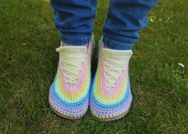Top view of pastel rainbow crochet lace-up slippers worn with rolled jeans on grass