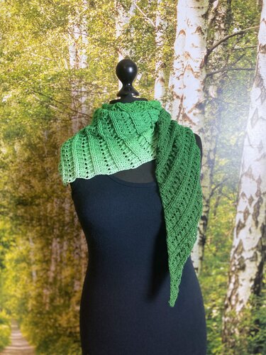 Asymmetric green gradient crochet triangle shawl on a black mannequin with a birch forest backdrop