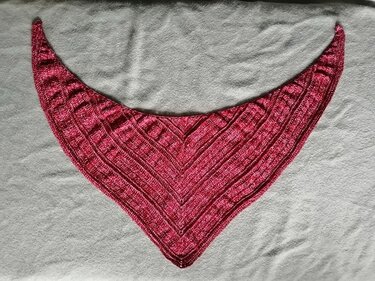 Handgehäkeltes Dreieckstuch in Rot‑Pink mit strukturierter Musterung auf hellgrauem Untergrund.