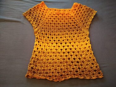 Gehäkeltes gelb-orange Damen-Shirt mit kurzem Ärmel und offenem Lochmuster, flach auf Stoff gelegt