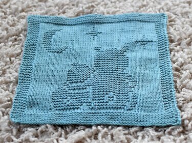 Light blue knitted square with garter-stitch cat silhouette, crescent moon and star