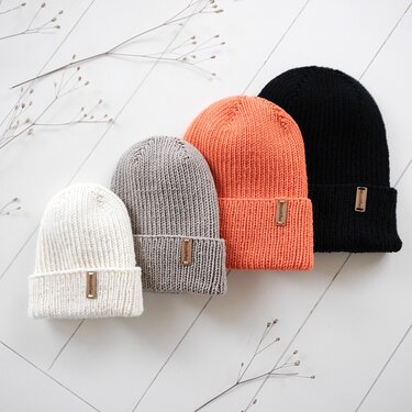 Vier gestrickte Beanies in Weiß, Grau, Orange und Schwarz in unterschiedlichen Größen.