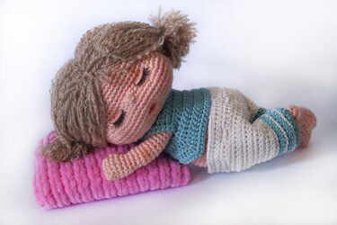 Gehäkelte schlafende Amigurumi‑Puppe liegend auf rosafarbenem Kissen