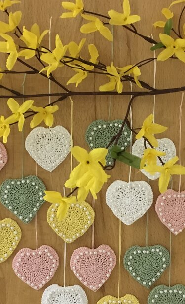 Gehäkelte Pastellherzen mit Perlen an gelben Forsythienzweigen