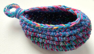 Gehäkelter kleiner bunter Korb mit Schlaufe auf hellem Hintergrund