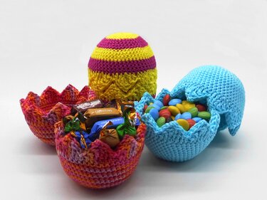 Geöffnete, bunte gehäkelte Ostereier, deren untere Hälften mit verschiedenen Süßigkeiten gefüllt sind