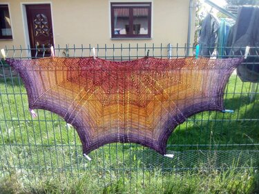 Gehäkeltes Tuch in Lila, Orange und Rotbraun mit Spitzen- und Lochmuster an einem Gartenzaun