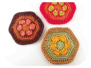 Drei gehäkelte sechseckige Applikationen mit Blumenmotiv in verschiedenen Farben