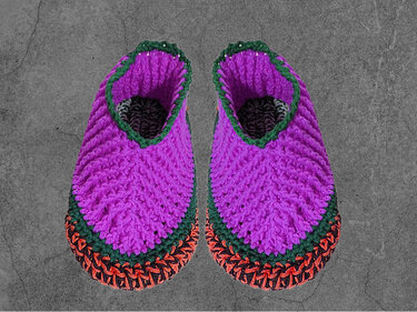 Gehäkelte Hausschuhe in Lila mit grünen und orangen Rändern auf grauem Hintergrund
