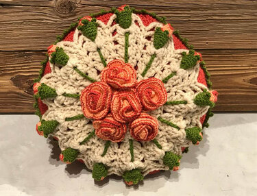 Nahaufnahme einer runden gehäkelten Kissenhülle mit orangefarbenen Rosen