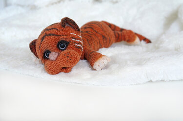 Gehäkelter orangefarbener Tiger mit dunklen Streifen auf weißer, flauschiger Decke