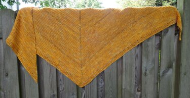 Senfgelbes gestricktes Dreieckstuch mit Lochreihen über einem Holzzaun